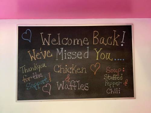 Chalkboard sign welcoming back customers, featuring "Chicken & Waffles" and "Stuffed Pepper & Chili" soup.