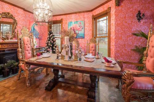 A vibrant dining room with pink floral walls, ornate chairs, a festive table setting, and a small Christmas tree.