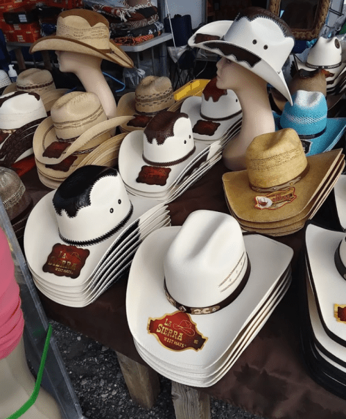A display of various cowboy hats in different colors and styles, arranged on a table with mannequin heads.