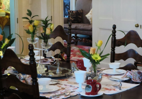 A beautifully set dining table with floral arrangements, elegant dishware, and a cozy room in the background.