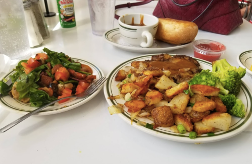 A plate of grilled meat with potatoes and broccoli, alongside a fresh salad and a cup of soup on a table.