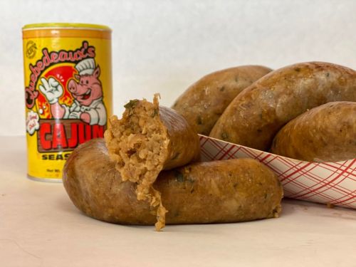 A close-up of sliced sausage with Cajun seasoning canister in the background and more sausage in a basket.