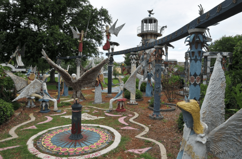 A whimsical outdoor sculpture garden featuring various angelic figures and a lighthouse amidst lush greenery.