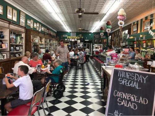 A bustling vintage diner with checkered floors, patrons enjoying meals, and a display of ice cream and old photos.