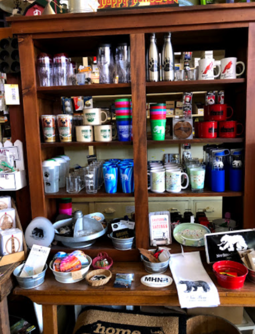A wooden display cabinet filled with various mugs, glasses, and souvenirs, featuring animal designs and colorful items.