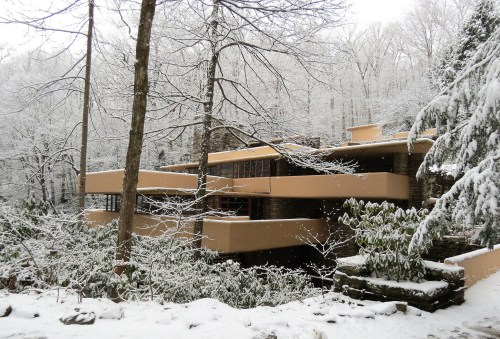 A modern house nestled in a snowy forest, surrounded by trees and blanketed in fresh snow.