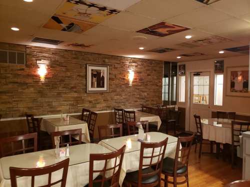 Cozy restaurant interior with stone walls, tables set for dining, and framed artwork on the ceiling.