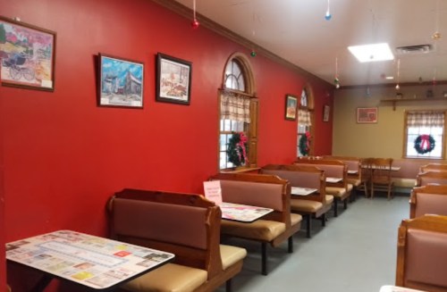 Cozy restaurant interior with red walls, wooden booths, festive decorations, and colorful artwork.