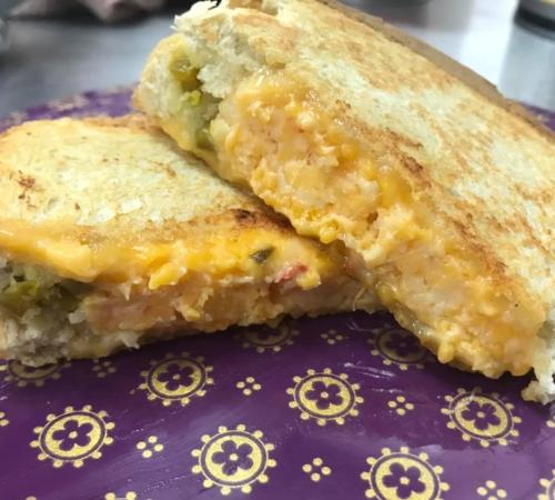 A close-up of a grilled cheese sandwich with melted cheese and a golden-brown crust, served on a decorative plate.
