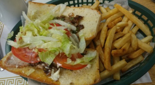 A sandwich filled with lettuce, tomatoes, and meat, served with a side of golden French fries in a green basket.