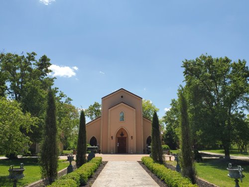 A charming building with a peaked roof, surrounded by lush greenery and tall trees under a clear blue sky.