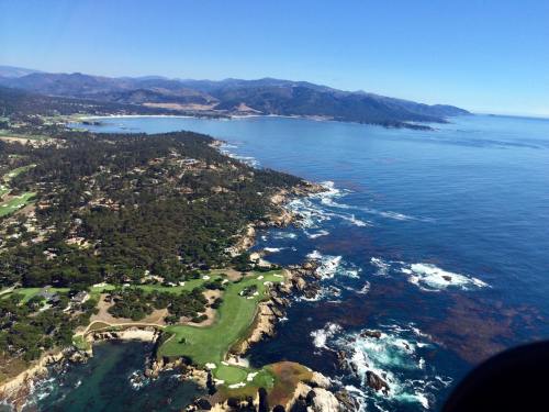 Aerial view of a coastal landscape featuring green golf courses, rocky shores, and blue ocean under a clear sky.