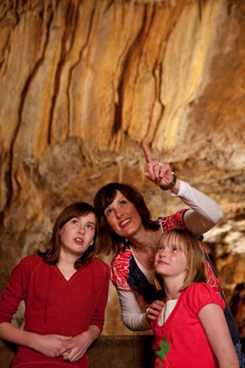 A woman and two girls explore a cave, looking up at the rock formations with curiosity and wonder.