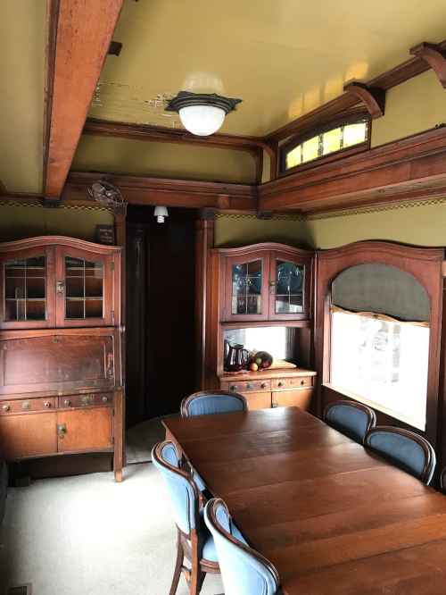 A vintage dining room with wooden furniture, a large table, and decorative cabinetry against a green wall.