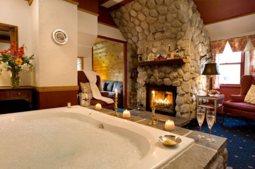 A cozy bathroom with a stone fireplace, a bubbling hot tub, candles, and elegant decor, creating a relaxing atmosphere.