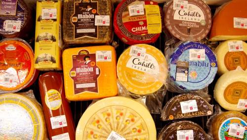 A variety of cheeses displayed on a table, each with price tags, showcasing different shapes and colors.