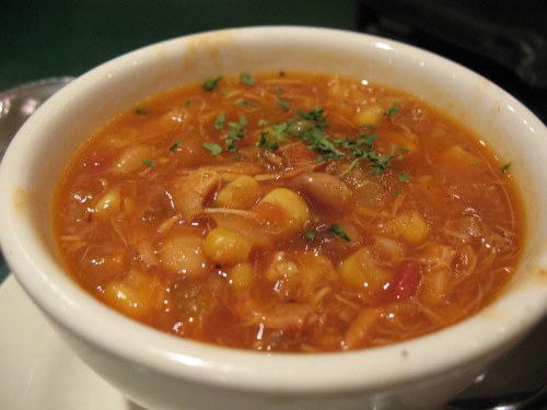 A bowl of hearty soup with beans, corn, and herbs, served on a white plate.