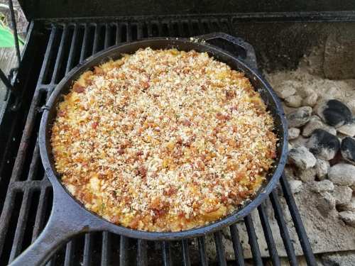 A cast iron skillet on a grill, filled with a baked dish topped with crispy breadcrumbs and herbs.