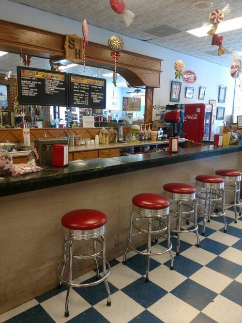 A retro diner interior featuring a counter with red stools, a menu board, and vintage decor.