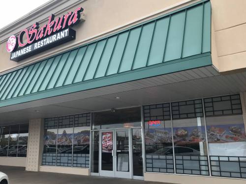 Exterior of Sakura Japanese Restaurant, featuring a green awning and large windows with a "Open" sign.