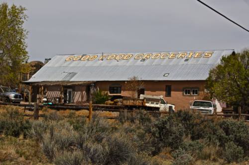 A rustic grocery store with a metal roof, featuring the sign "Good Food Groceries" and surrounded by sparse vegetation.