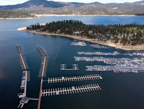 Aerial view of a marina with numerous boat docks, surrounded by water and mountains in the background.