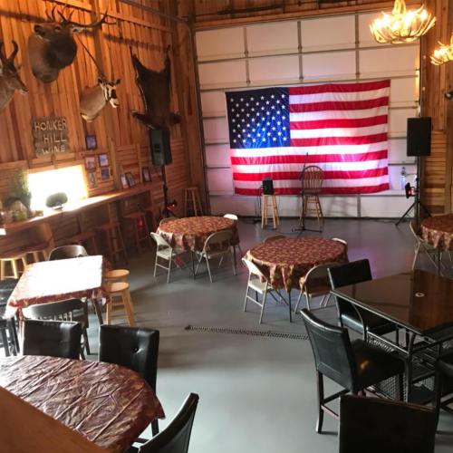 A rustic venue with tables, chairs, and an American flag backdrop, ready for an event or performance.