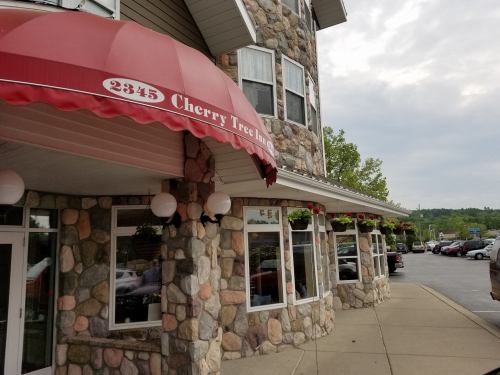 Exterior of Cherry Tree Inn, featuring a stone facade, red awning, and flower planters, with parked cars nearby.