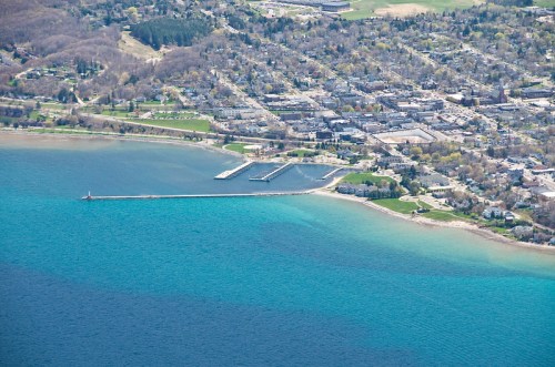 Aerial view of a coastal town with a marina, green parks, and clear blue water.