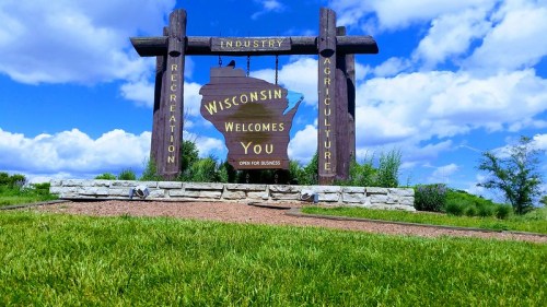 Sign welcoming visitors to Wisconsin, highlighting industry, recreation, and agriculture, set against a blue sky.