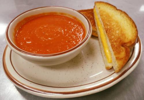 A bowl of tomato soup next to a grilled cheese sandwich on a plate.