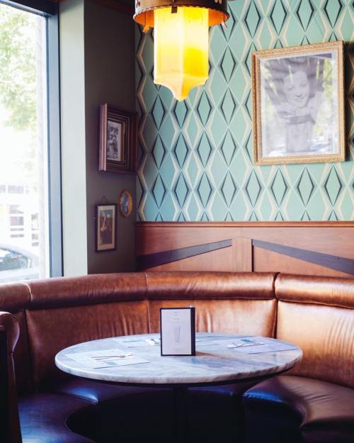 Cozy café corner with a round marble table, leather seating, and vintage decor, including a framed portrait on the wall.