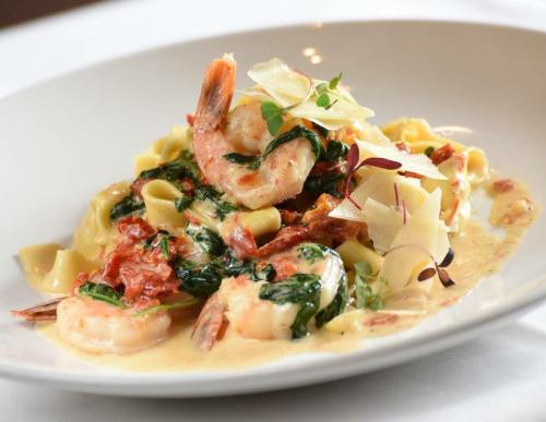 A plate of creamy pasta with shrimp, spinach, sun-dried tomatoes, and shaved Parmesan cheese.