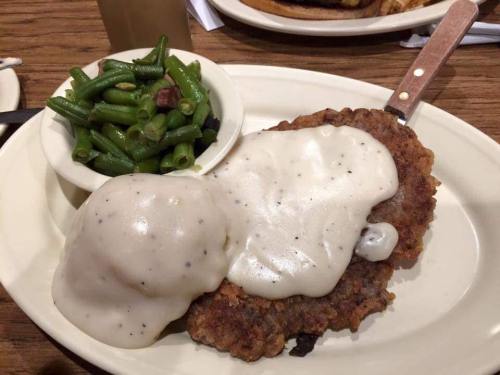 A plate featuring a breaded meat patty topped with creamy gravy, served with mashed potatoes and green beans on the side.
