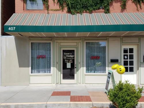 A storefront with a green awning, "Sam's Fudge" sign, and open hours displayed. Smiley balloon outside.