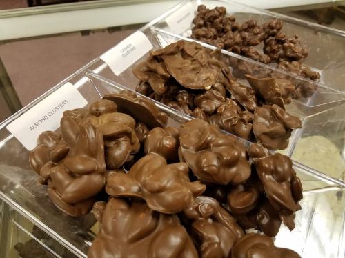 A display of chocolate clusters, including almond clusters, in clear containers.