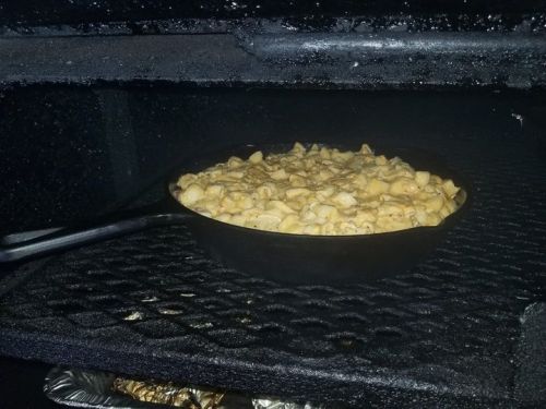 A cast iron skillet filled with macaroni and cheese inside a smoker, resting on a grill rack.