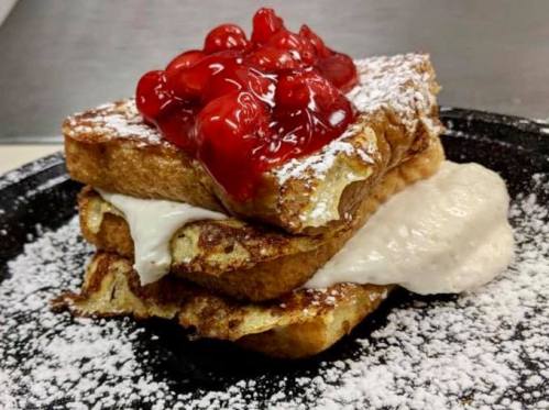 Stack of French toast topped with cherry filling and powdered sugar, with a creamy filling peeking out between the layers.