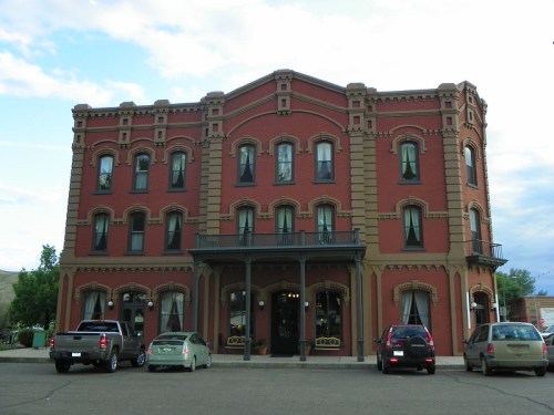 Historic red brick building with ornate architecture, featuring large windows and parked cars in front.