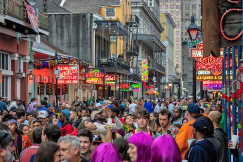 A bustling street in New Orleans filled with crowds, colorful signs, and festive decorations during a celebration.