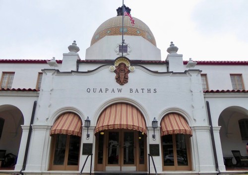 Historic Quapaw Baths building with a dome, arched windows, and striped awnings, located in a scenic area.