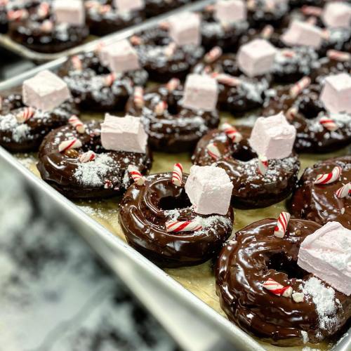 A tray of chocolate-covered donuts topped with marshmallows and peppermint candies, dusted with powdered sugar.