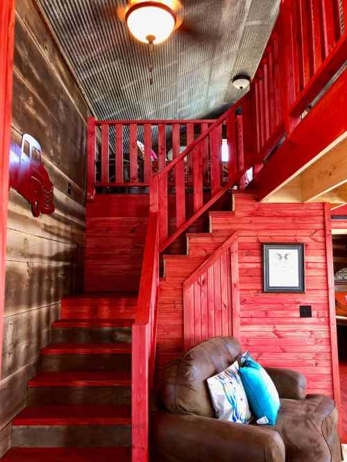 A cozy interior featuring red wooden stairs, a brown couch, and rustic walls with a vintage truck decoration.