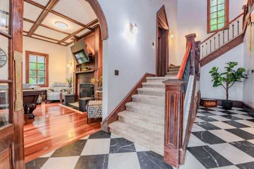 A spacious entryway with a staircase, checkered floor, and a view of a cozy living area with a fireplace.