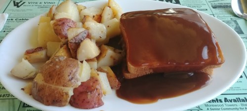 A plate with roasted potatoes and a slice of bread topped with brown gravy.