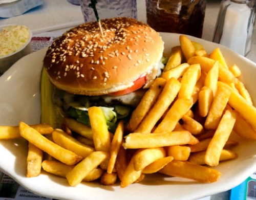 A sesame seed bun burger with lettuce, tomato, and pickles, served with a side of golden French fries.