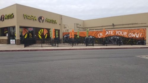 Exterior of Pizza Artist with colorful mural and outdoor seating, featuring "Create Your Own" text on the wall.