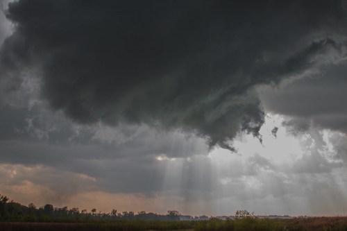Dark storm clouds loom over a landscape, with rays of sunlight breaking through the clouds.