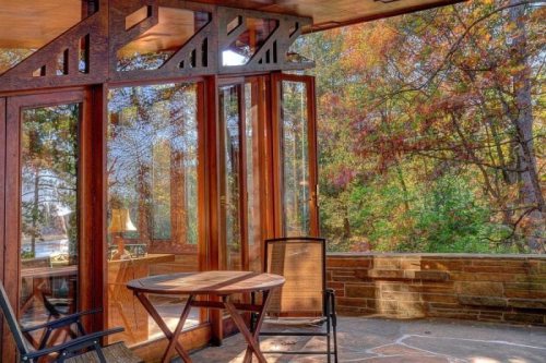 Cozy sunroom with wooden accents, a table, and chairs, surrounded by colorful autumn foliage.