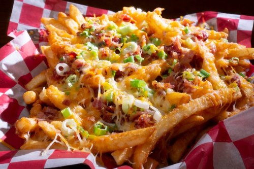 A basket of loaded fries topped with cheese, bacon, and green onions on a red and white checkered paper.